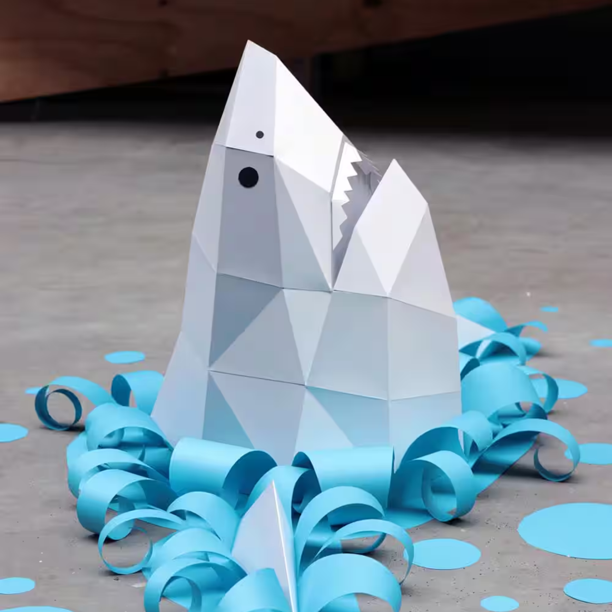 Grijze Assembli 3D-puzzel haaienkop op de grond met papieren golven in het blauw erom heen 