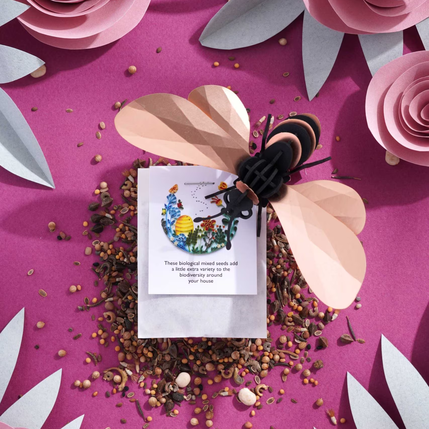 Bovenaanzicht van de Assembli papieren honingbij rose goud met bijgeleverde zakje bloemenzaden op een paarse achtergrond.